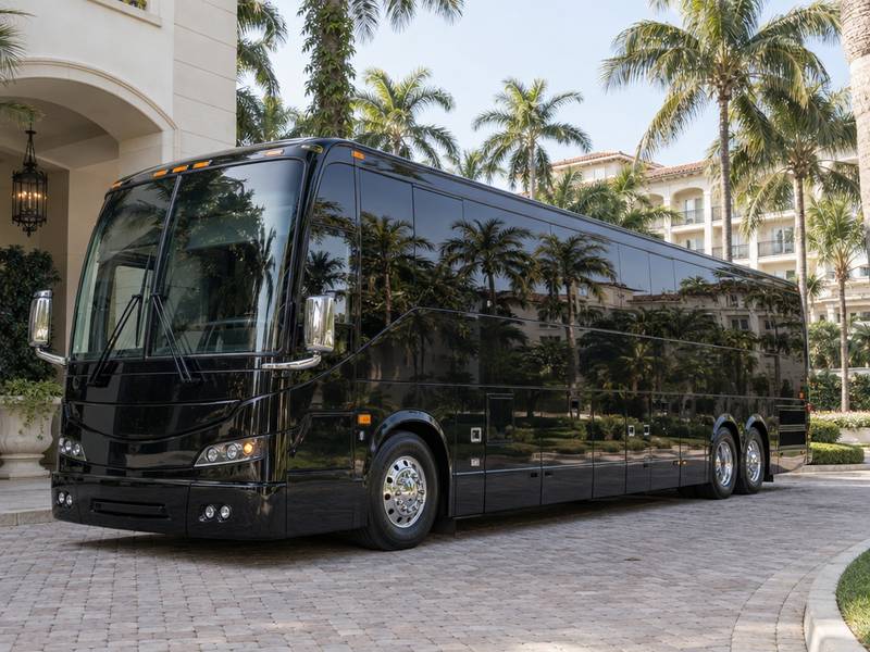 Black luxury motorcoach at a palm-lined resort entrance